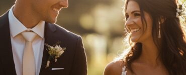 An elegant bride and groom holding hands, smiling as they walk through a sunlit garden, with a soft-focus background.
