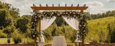 An outdoor wedding ceremony under sunny skies, featuring a scenic natural backdrop with greenery and flowers, rows of chairs for guests, and a beautifully decorated arch at the altar. The atmosphere is warm and inviting, perfect for a dreamy celebration surrounded by nature.