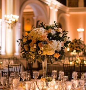 Wedding reception setup with elegant tables, floral centerpieces, and soft lighting in a grand venue.