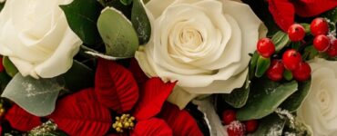 A beautiful winter wedding bouquet featuring white roses, red poinsettias, and lush greenery, symbolizing elegance and seasonal charm.