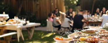 A sunny backyard engagement party setup with a table of food, string lights, and friends and family gathered in celebration.