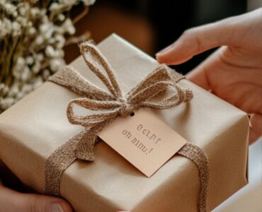 Close-up of hands exchanging a beautifully wrapped gift with a ‘Congrats on the engagement!’ tag, symbolizing thoughtful celebration of a couple's milestone.