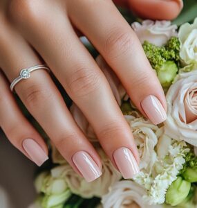 Close-up of a bride’s hands with freshly manicured nails resting on her wedding bouquet, showcasing soft pink nail polish with a glossy finish.