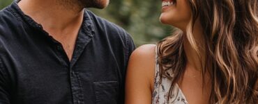 A couple holding hands and smiling lovingly at each other in an intimate, natural setting.