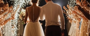 An elegant wedding couple exiting through an archway of lights, surrounded by cheering guests.
