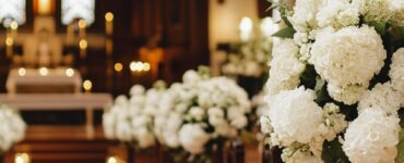 Elegant church interior decorated with white floral arrangements and candles along the aisle, complementing the traditional stained glass windows.