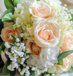 A photo of a beautifully arranged wedding bouquet made from artificial flowers, including roses, hydrangeas, and baby’s breath, resting on a white lace cloth.