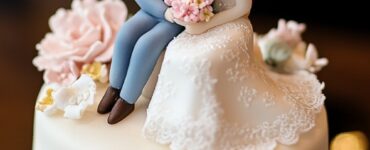 Close-up of a small wedding cake topped with a charming bride and groom figurine, surrounded by delicate floral decorations.