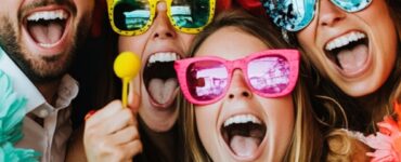 A fun and vibrant DIY wedding photo booth setup with guests laughing, posing with props, and capturing memorable moments.