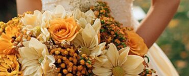 Bride holding a bouquet of fall flowers, including vibrant orange, yellow, highlighting an autumn-inspired color palette.