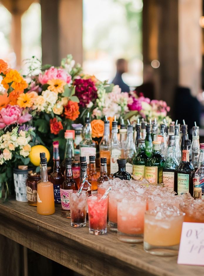 A DIY bar at a wedding reception with a variety of drinks, mixers, and cocktail recipe cards for guests to create their own cocktails.