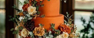 A stunning wedding cake decorated with burnt orange fondant and fresh flowers, accented with metallic gold and deep green, perfect for a fall-themed wedding.