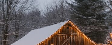 A serene rustic winter wedding setup featuring a snowy barn adorned with warm string lights and surrounded by frosty trees.