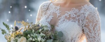 An elegant winter bride standing in a snowy landscape, wearing a lace gown and holding a bouquet, surrounded by soft twinkling lights and a serene backdrop.