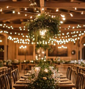 Rustic indoor wedding venue with warm string lights, wooden accents, and cozy greenery decorations, creating an elegant and intimate ambiance.