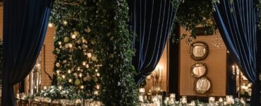 Elegant winter wedding decor featuring green and navy blue accents, including lush greenery, navy drapes, and glowing candlelight to set a timeless seasonal ambiance.