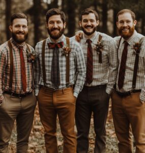 Rustic groomsmen standing outdoors in nature, dressed in a variety of outfits like suspenders, plaid shirts, and earth-toned suits, showcasing vintage-inspired rustic wedding attire.