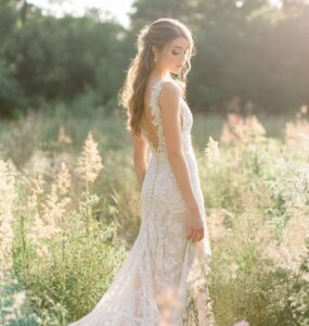 A bride in a rustic outdoor wedding setting wearing a lace wedding dress, surrounded by nature, with a soft, romantic glow.