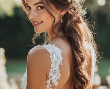 An elegant bride standing in a rustic outdoor wedding setting, her hairstyle reflecting natural beauty with soft waves and floral accents, complementing the countryside charm.