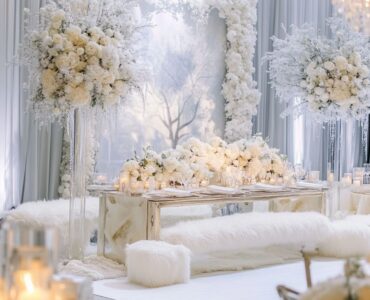 An elegant white winter wedding setup featuring a snowy backdrop, white floral arrangements, and cozy faux fur accents, creating a magical and serene atmosphere for a winter wonderland celebration.