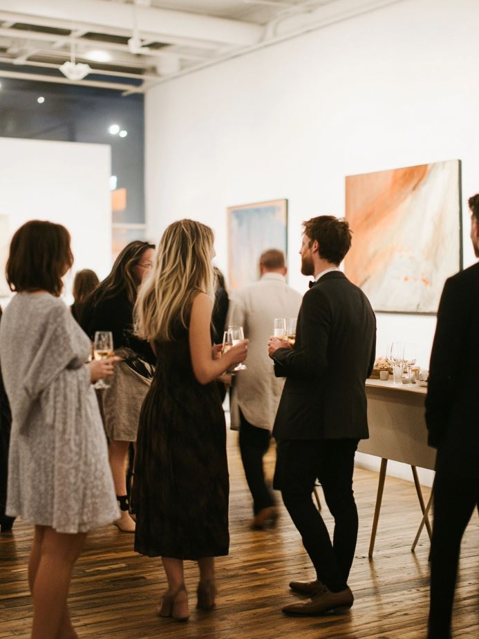 Elegant art gallery wedding reception with guests mingling among art pieces, sipping champagne, and enjoying appetizers in a minimalist setting.