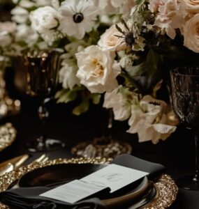 An elegant wedding table setting featuring black linens, gold-rimmed dinnerware, and romantic floral arrangements, showcasing the timeless sophistication of black wedding palettes.