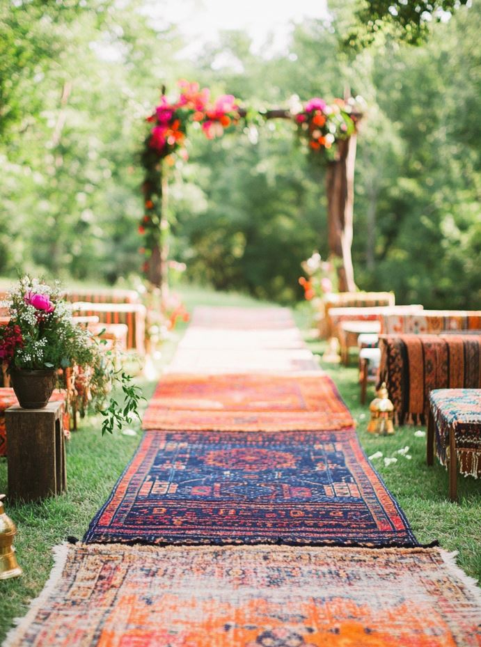 Colorful, patterned bohemian rugs create a cozy and eclectic path for guests to walk along, adding a unique and artistic touch to a backyard wedding.