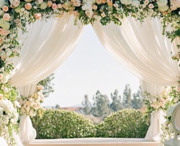 An elegant outdoor spring wedding ceremony setup featuring pastel florals, greenery, and soft draped linens under clear skies.
