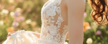 A bride twirls in a soft lace wedding dress with floral appliqués, surrounded by pastel-colored spring blooms and a dreamy, golden sunset in the background.