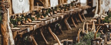 A captivating Viking wedding setup featuring a rustic wooden arch with runes, a long feast table with horn accents, Nordic lanterns, antler centerpieces, and runestone-inspired signage, blending history and romance for a magical celebration.