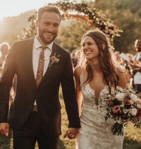 Image of a newlywed couple walking hand-in-hand through a scenic backdrop, with a personalized wedding arch behind them and joyous guests celebrating in the background.