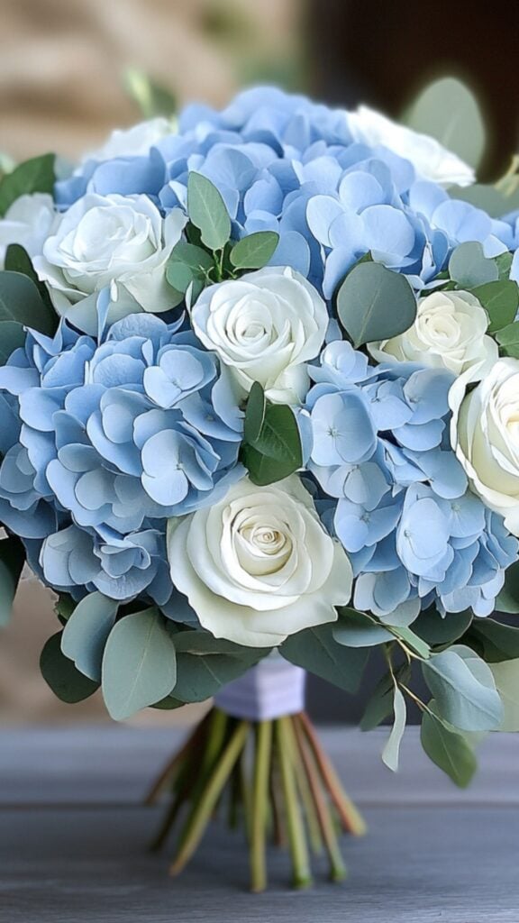 A bouquet of blue hydrangeas with full, rounded blooms, arranged with white roses and eucalyptus for a romantic wedding setting.