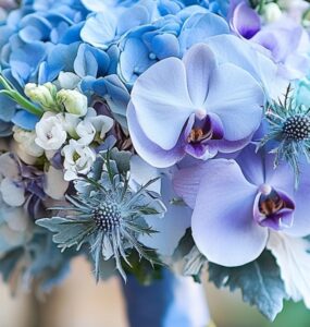 A close-up of an elegant blue wedding bouquet resting on a table, featuring a mix of hydrangeas, orchids, and thistles, symbolizing timeless wedding charm.