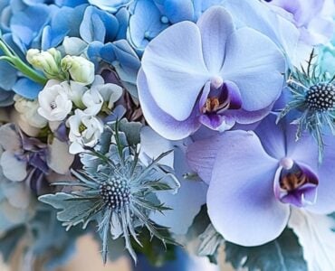 A close-up of an elegant blue wedding bouquet resting on a table, featuring a mix of hydrangeas, orchids, and thistles, symbolizing timeless wedding charm.
