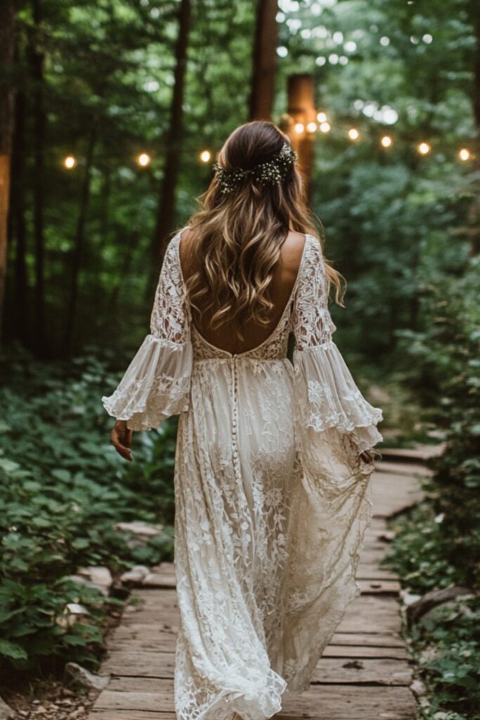 A bohemian bride in a flowing lace gown with bell sleeves and floral embroidery, walking barefoot on a rustic outdoor path surrounded by greenery and string lights.