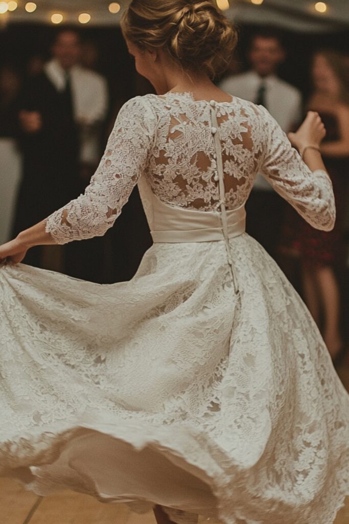 A bride in a vintage-inspired tea-length dress, featuring a cinched waist and lace sleeves, playfully twirling on the dance floor with her heels visible.