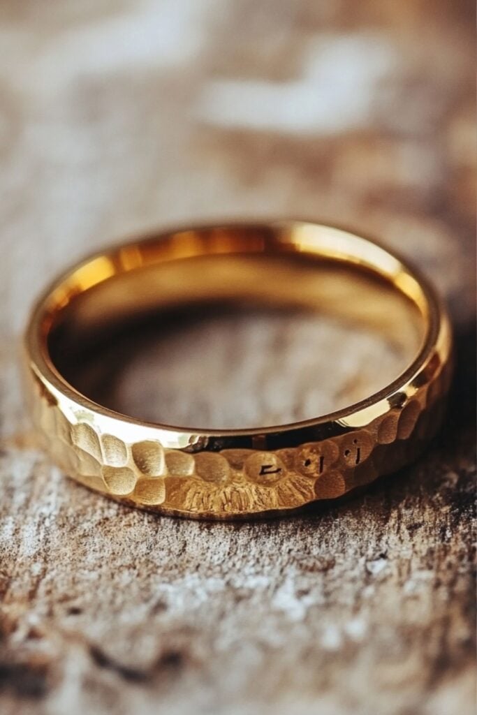 Gold wedding ring with a personalized engraving on the inside and a hammered texture on the outside, shown resting on a wooden surface.