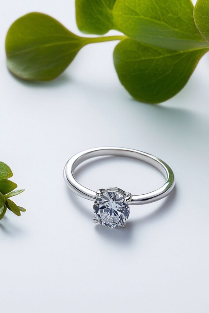 Lab-grown diamond ring with a recycled platinum band, displayed next to small green leaves, symbolizing sustainability.