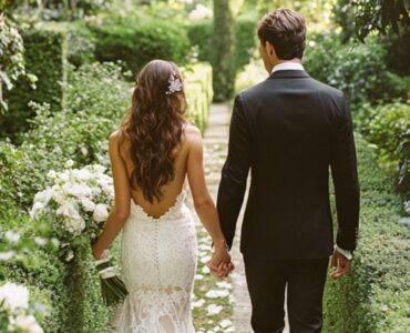 Bride and groom walking hand in hand down a garden aisle lined with greenery, symbolizing a timeless and elegant green wedding color palette.