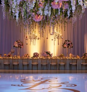 Elegant wedding reception scene with a custom monogrammed dance floor, floral backdrop, and ambient lighting, showcasing personalized and modern decor touches.