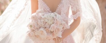 Bride in a soft pink gown walking down the aisle, surrounded by guests, with a radiant smile and a long flowing veil trailing behind.
