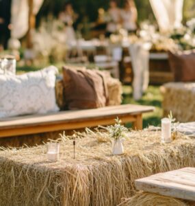 A close-up of a rustic wedding seating arrangement featuring a mix of styles, including hay bales, wooden benches, and vintage chairs, set against a serene outdoor backdrop.