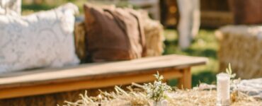 A close-up of a rustic wedding seating arrangement featuring a mix of styles, including hay bales, wooden benches, and vintage chairs, set against a serene outdoor backdrop.