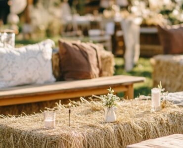A close-up of a rustic wedding seating arrangement featuring a mix of styles, including hay bales, wooden benches, and vintage chairs, set against a serene outdoor backdrop.