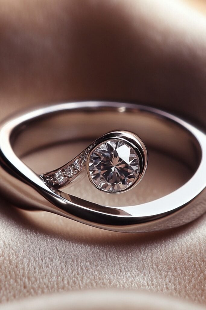 An asymmetric wedding ring with an open-ended design and offset gemstone, shown against a soft velvet background.