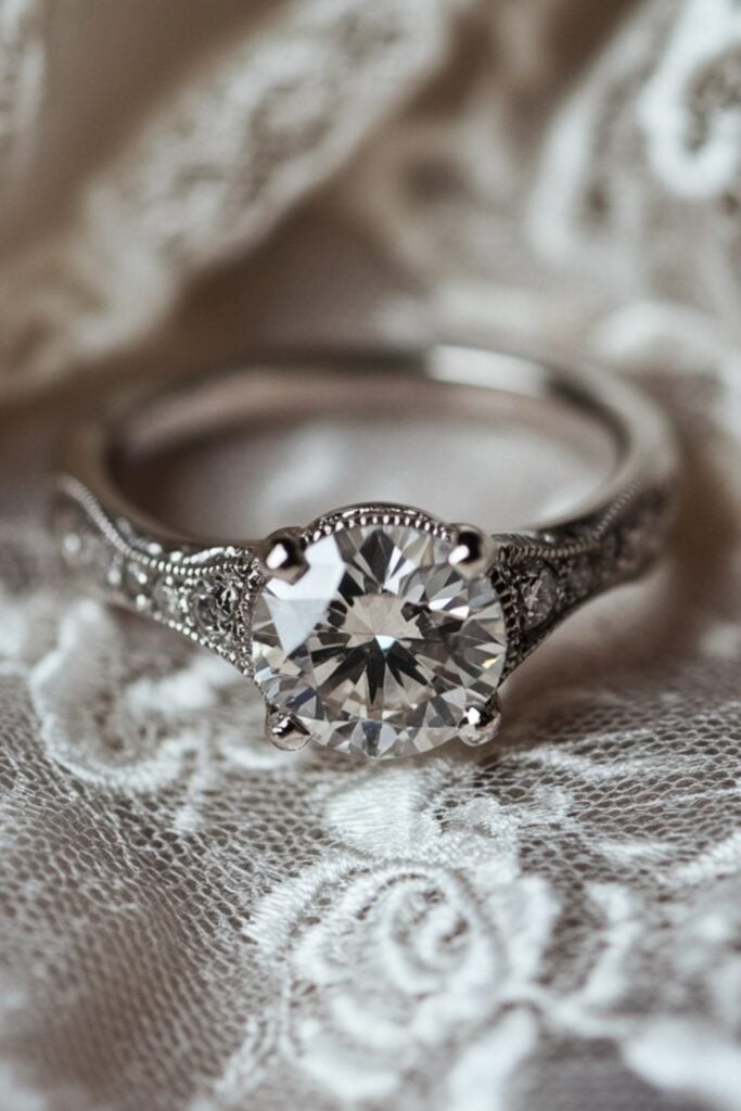 Vintage-style wedding ring with intricate milgrain detailing and a unique salt-and-pepper diamond at the center, displayed on a lace fabric.