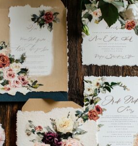 A beautifully styled backyard wedding invitation with floral designs and elegant calligraphy, set on a rustic wooden table.