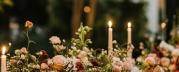 A beautifully decorated backyard wedding table featuring floral arrangements, candles, and elegant tableware, set in a lush outdoor setting with string lights overhead.