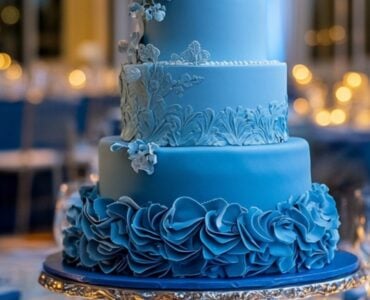 A beautifully designed blue wedding cake displayed at a reception, surrounded by elegant décor, candles, and floral arrangements, ready to impress guests.