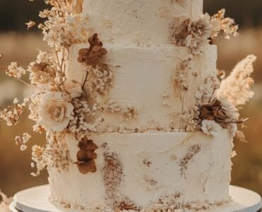 A beautiful boho wedding cake displayed at a dreamy outdoor reception, featuring rustic textures, dried florals, and elegant handmade details.